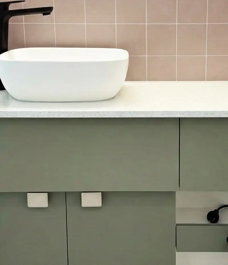 Il paraschizzi chiaro dietro un piano con un lavabo, in un bagno di camper.