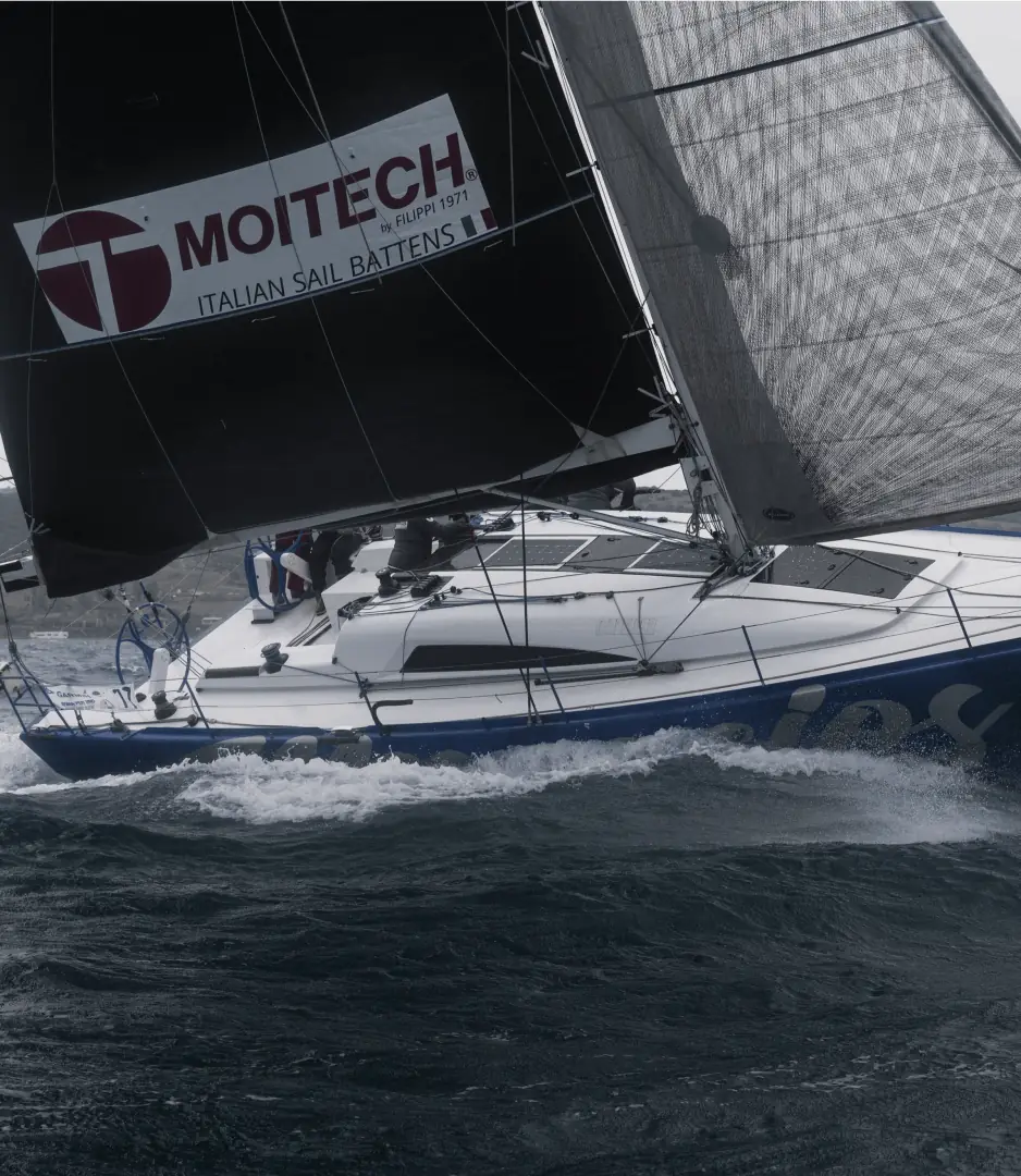 Una barca a vela da regata col logo Moitech sulla vela, in mezzo alle onde.